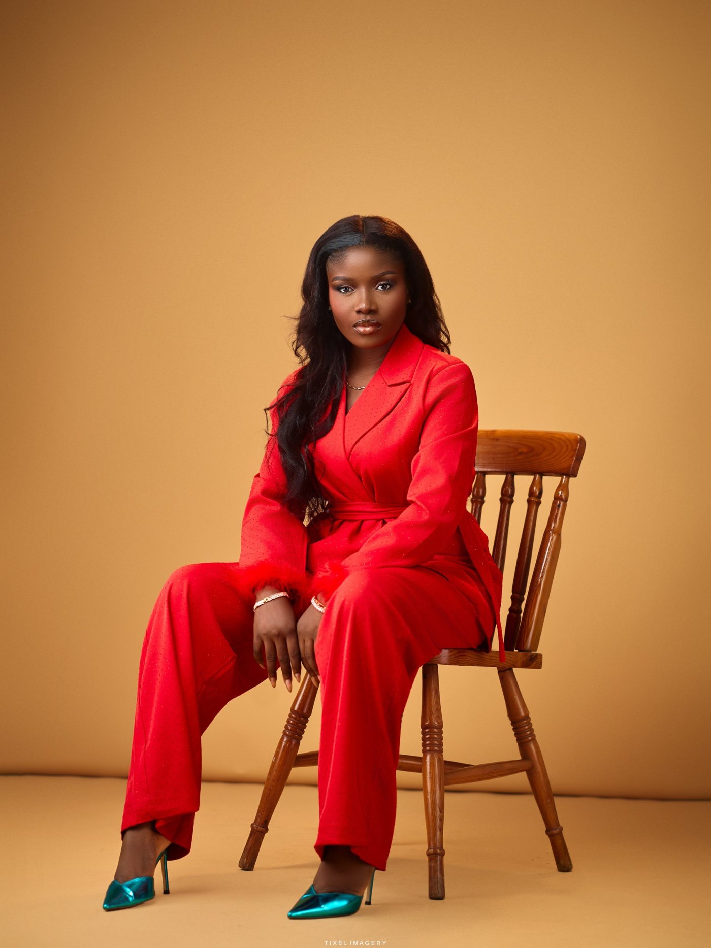 Sarah Adesemoye, founder of Shinne, seated in a red tailored set.